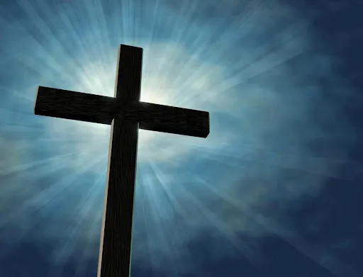 Silhouette of a wooden cross against a bright sky with sunbeams radiating from behind it.